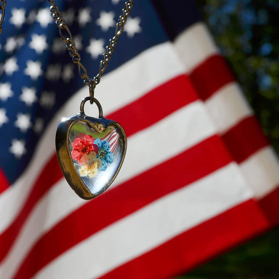 Handmade Red White and Blue Pressed Flower Heart Pendant Necklace with American Flag in background. Truly Handmade in USA by Louisiana Artisan at Bayou Glass Arts Studio. Forget Me Nots