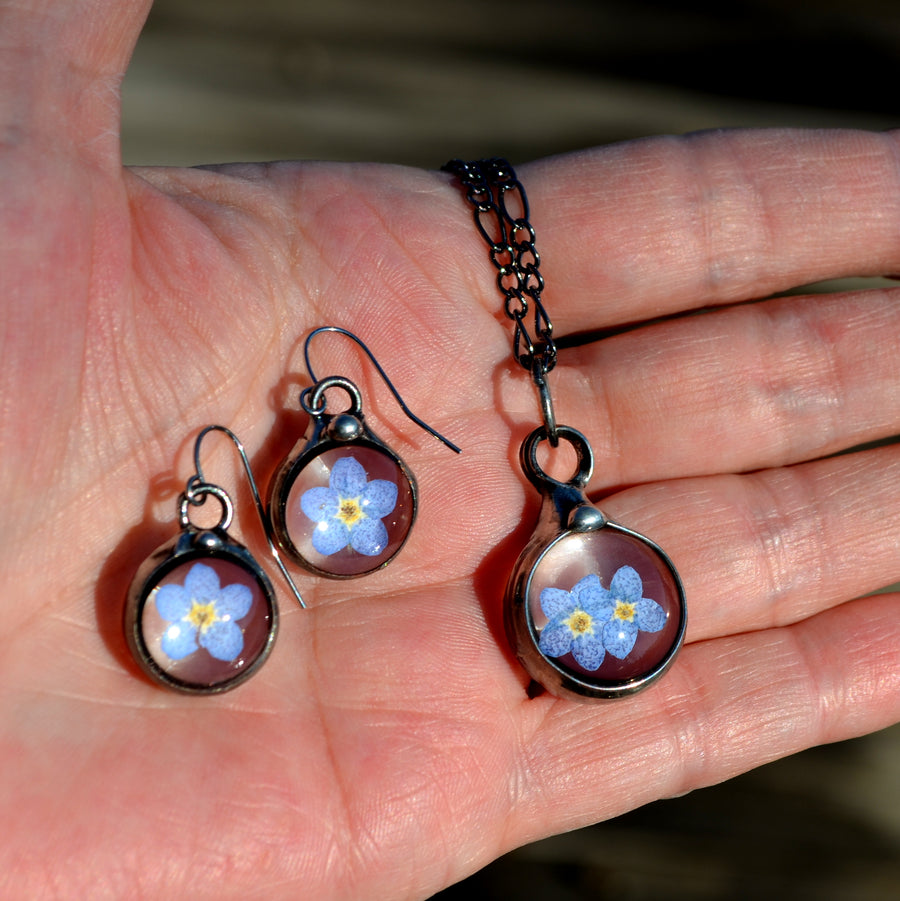Forget me not earrings on sterling silver ear wires shown next to a 2 bloom pendant. One blue bloom inside each round glass earring, bezel is hand formed with copper and mixed silver solder by Louisiana Artisan. Hand made in USA.