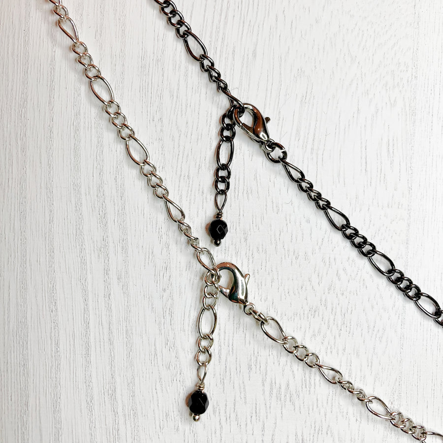 Two figaro chains side by side to compare the color and finish. Gunmetal/Shiny Black or Shiny Silver. Notice the chain can be changed to any length by using alternate links in the figaro chain, also the elegant dangling glass czech bead when shortening necklace is done. 