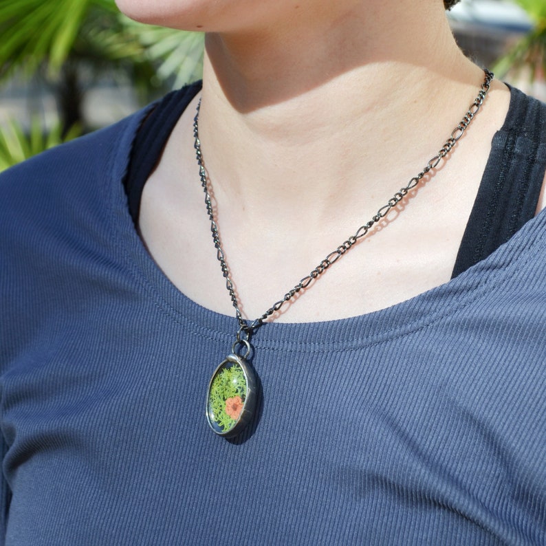 model wearing green moss pendant with orange flower, pressed flower terrarium jewelry