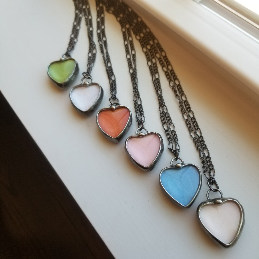 6 different colors of See See Heart Pendant Necklaces: Green, White, Orange, Pink, Blue, Peach.See See Jewelry is hand made in USA by Louisiana Artisan at Bayou Glass Arts Studio. Secret message hidden inside is revealed when the pendant is held up to a light.