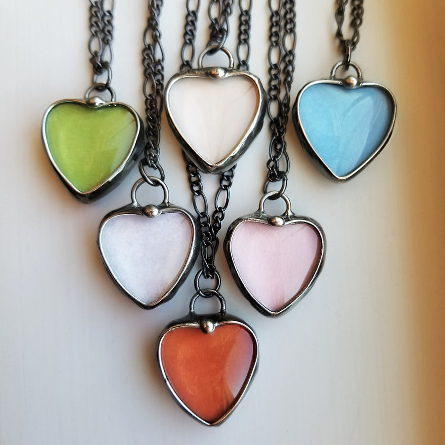 6 different colors of See See Heart Pendant Necklaces: Green, Peach, Blue, White, Pink, Orange. See See Jewelry is hand made in USA by Louisiana Artisan at Bayou Glass Arts Studio. Secret message hidden inside is revealed when pendant is held up to a light.