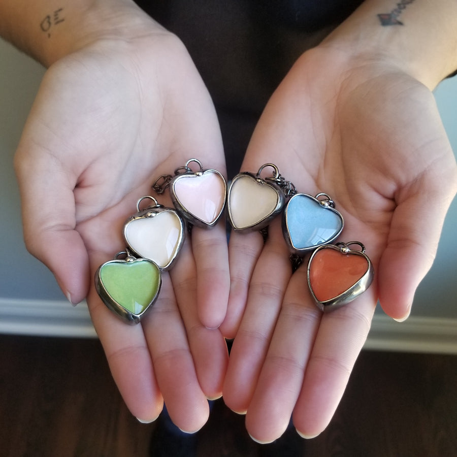 6 different colors of See See Heart Pendant Necklaces: Green White Pink Peach Blue Orange.See See Jewelry is hand made in USA by Louisiana Artisan at Bayou Glass Arts Studio. Secret message hidden inside is revealed when  the pendant is held up to a light.