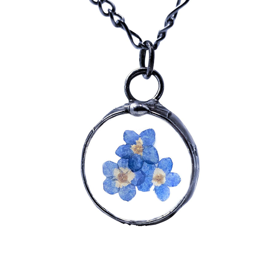 Handmade Pressed Flower Forget Me Not Pendant Necklace on white background. 3 Blue Blooms grace this delicate pendant that is round and comes in gunmetal or shiny silver finish. All Jewelry is Hand Made in USA by Louisiana Artisan at Bayou Glass Arts Studio.