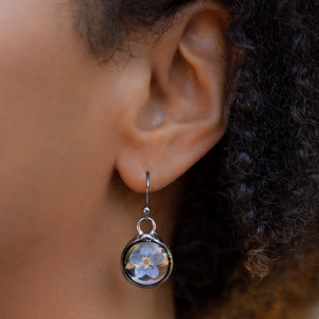 Forget me not earrings on sterling silver ear wires shown on model. One blue bloom inside each round glass  earring, bezel is hand formed with copper and mixed silver solder by Louisiana Artisan. Hand made in USA.