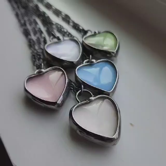 video of 5 colors of See See Heart Pendant Necklaces, White, Green, Pink, Blue, Peach.See See Jewelry is hand made in USA by Louisiana Artisan at Bayou Glass Arts Studio. Secret message hidden inside is revealed when pendant is held up to a light.