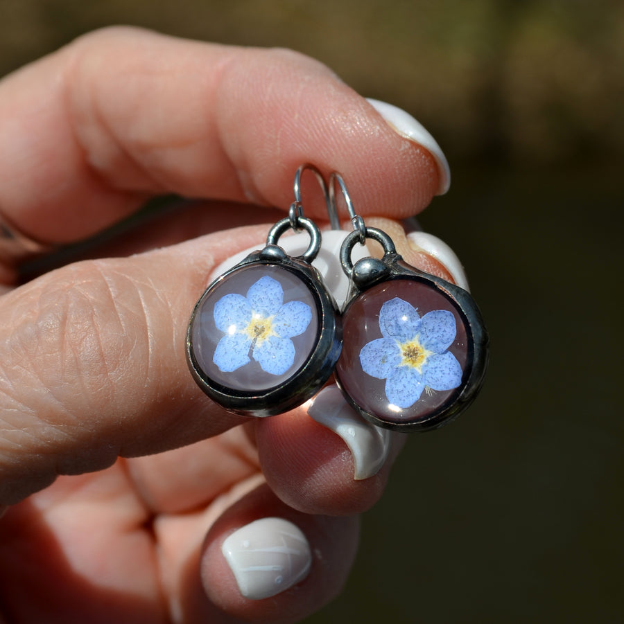 Forget me not earrings on sterling silver ear wires. One blue bloom inside each round glass earring, bezel is hand formed with copper and mixed silver solder by Louisiana Artisan. Hand made in USA.