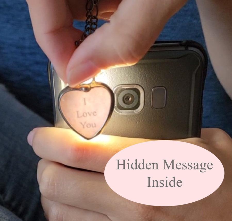 Handmade Pink Heart pendant being held close to flashlight to show the hidden message, I Love You. Secret message keepsake jewelry