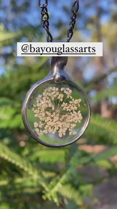 Video of Natural Queen Annes Lace Pendant, Real Pressed Wild flowers in glass necklace with gunmetal/shiny black bezel. Hand Made in USA by Artisans at Bayou Glass Arts in Louisiana.