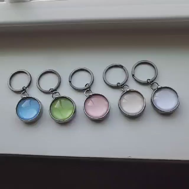 Video of 5 See See Round Key Rings in Assorted colors: Blue Green Pink Peach White. Truly Created and Hand Made in USA by Louisiana Artisan at Bayou Glass Arts Studio. See See Jewelry is designed so that it is a beautiful piece of jewelry and when you hold it up to a light, a hidden secret message is revealed inside.