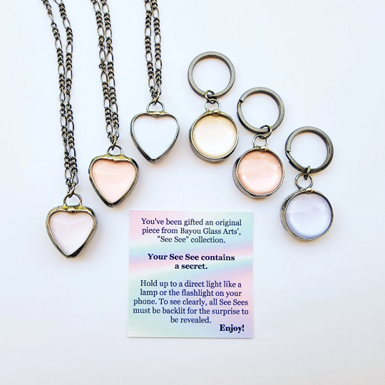 3 See See Heart Pendant Necklaces and 3 Round See See Key Rings with the gift card that accompanies each piece of See See Jewelry describing how it works, by holding a light behind it to reveal the message inside. Truly Hand Made in USA By Louisiana Artisan at Bayou Glass Arts Studio.