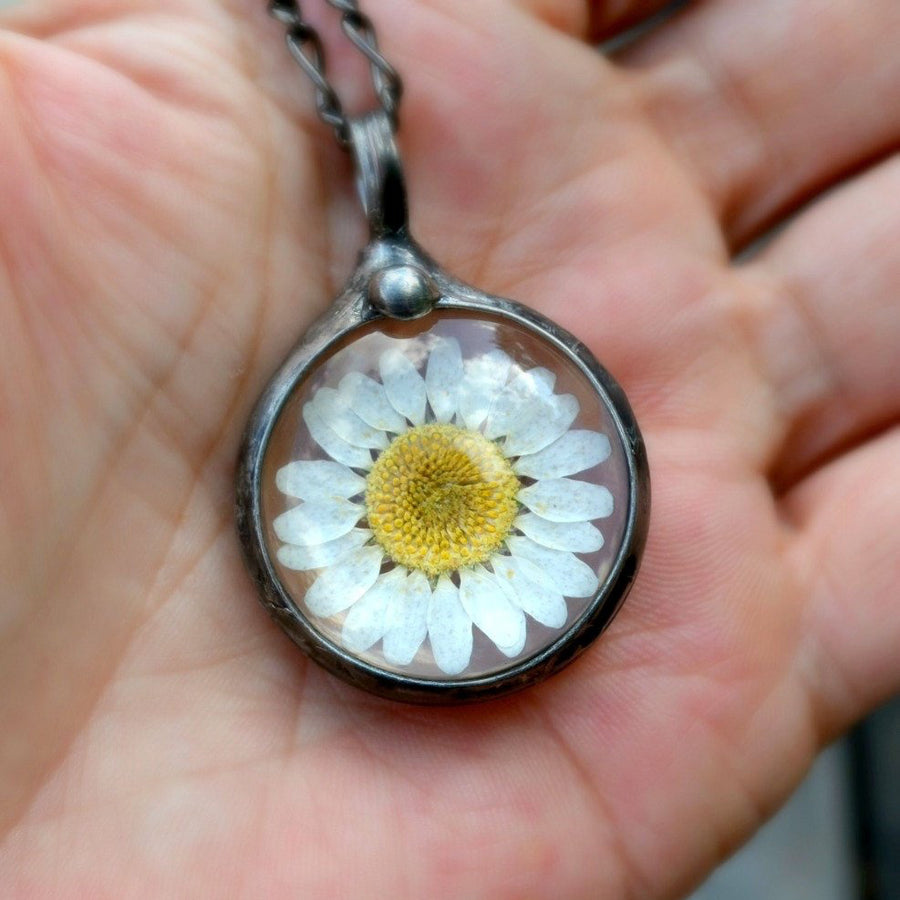 real dry pressed flower daisy in glass round pendant necklace held in hand. Truly hand made in USA by Louisiana artisan at Bayou Glass Arts studio.