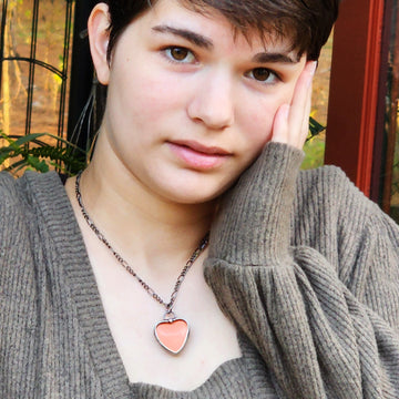 model wearing Orange Handmade See See Heart Pendant Necklace. Hold this pendant up to a bright light to reveal its message hidden inside. This one says I Love You in it.