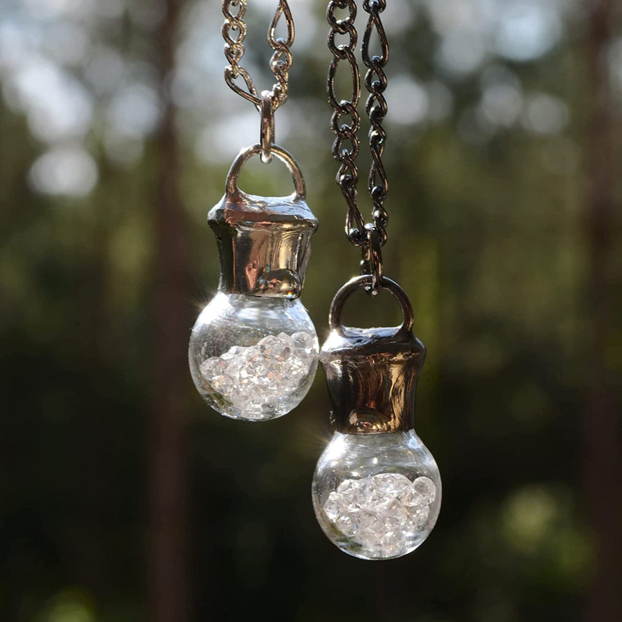 2 hand blown bottle pendants filled with crystals on Left has shiny silver finish, Right has gunmetal shiny black finish. Truly hand made in USA by Louisiana Artisans at Bayou Glass Arts Studio.  
