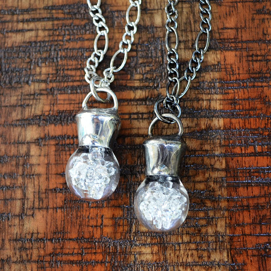 2 hand blown bottle pendants filled with crystals on Left has shiny silver finish, Right has gunmetal shiny black finish.  Truly hand made in USA by Louisiana Artisans at Bayou Glass Arts Studio. 
